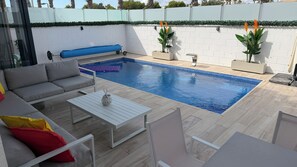 Ein Poolbereich mit einer weißen Wand, einem blauen Pool und einem grauen Sofa mit roten Kissen.