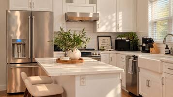 A modern kitchen with white cabinetry, stainless steel appliances, a central island with seating, and a view of the outdoors through a window.