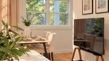 A dining area with a table set for four, a vase with flowers, and a television on a stand.