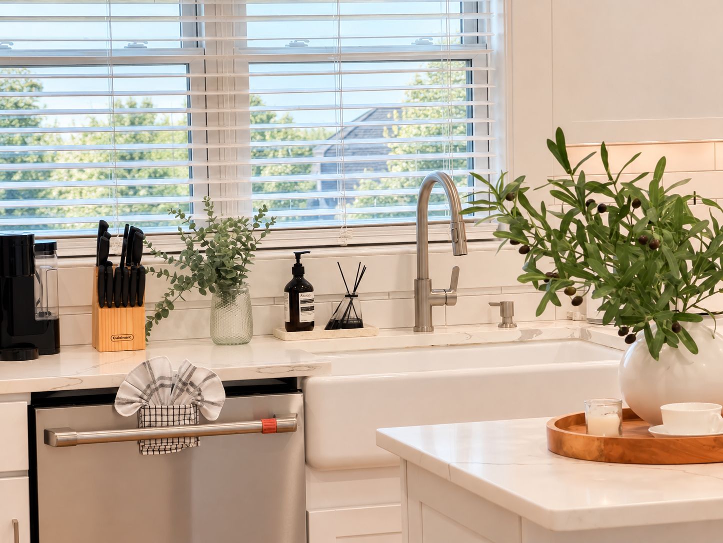 A modern kitchen with a built-in dishwasher, a stainless steel sink, and a window with blinds.