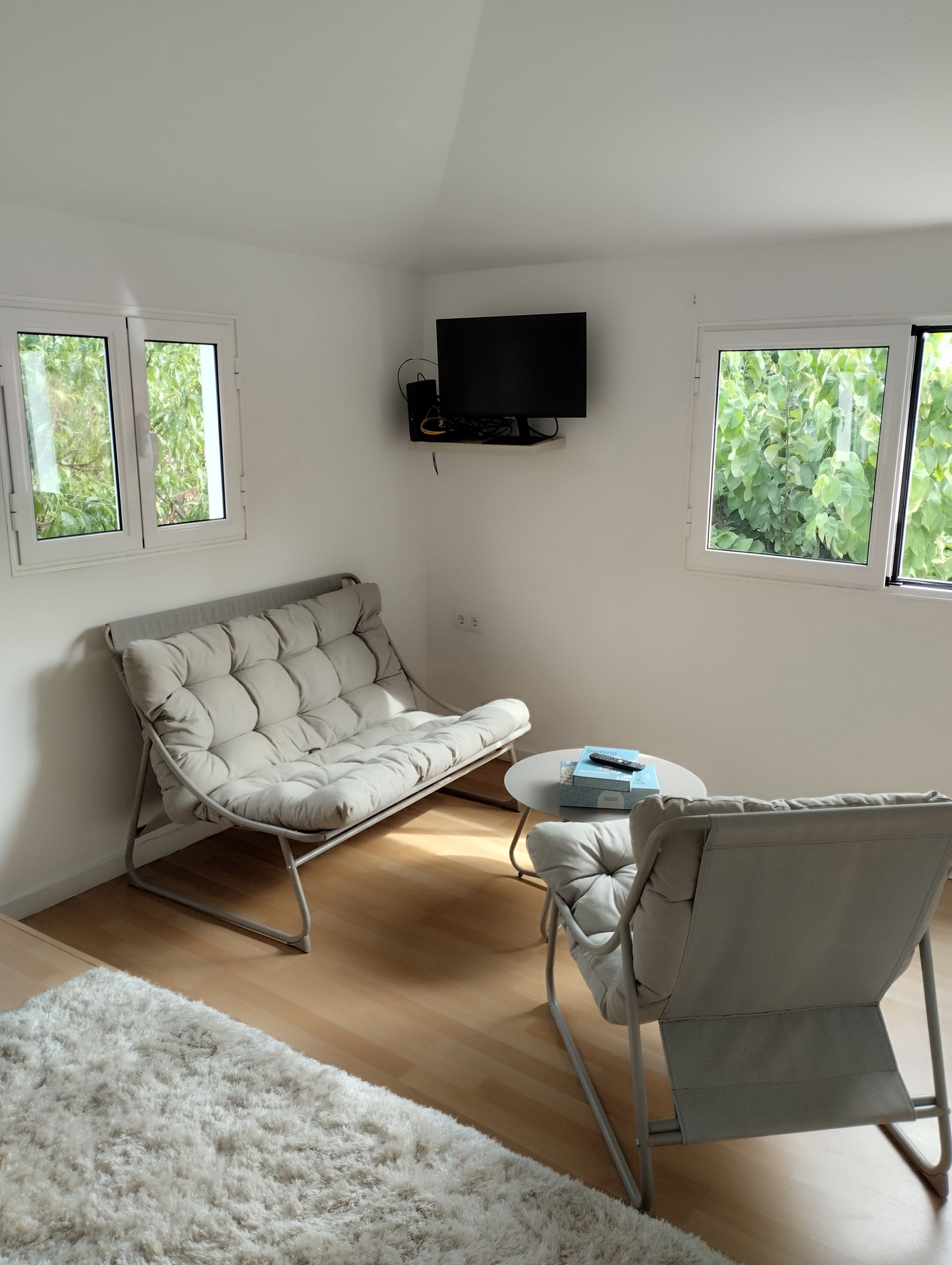 Une pièce comprenant un canapé-lit, un fauteuil, une petite table et un téléviseur fixé au mur.
