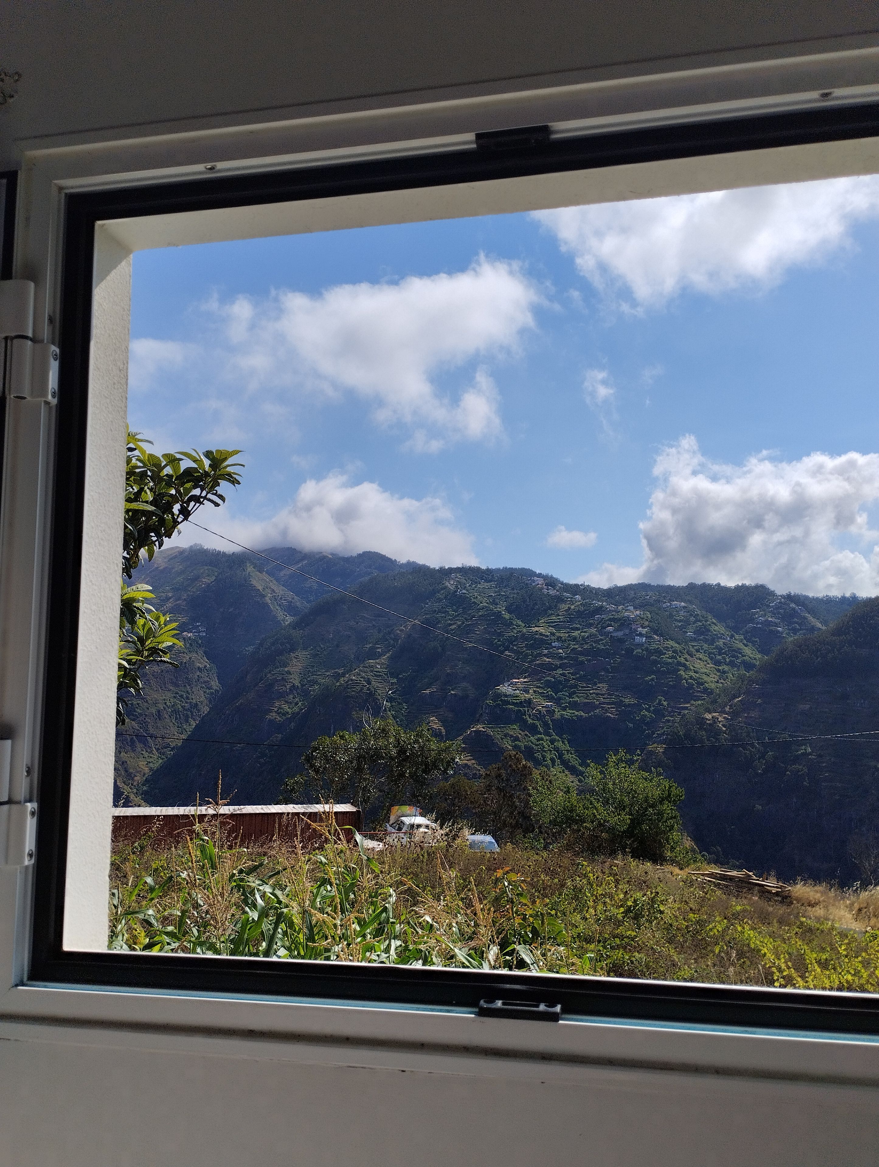 Une vue par la fenêtre sur un paysage montagneux, avec une végétation luxuriante et un ciel dégagé.