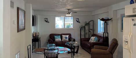 A spacious living area with a dining table, two sofas, and a ceiling fan.