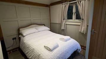 A bedroom with a bed, a window with curtains, a door, and a wooden floor.