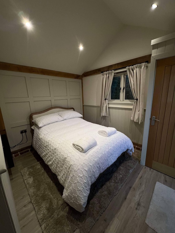 Un dormitorio con cama, ventana con cortinas, una puerta y piso de madera.