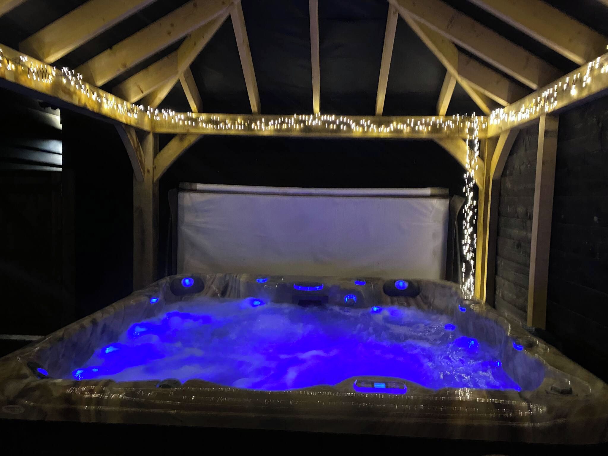 Banyera d'hidromassatge amb il·luminació blava a l'interior d'una estructura de fusta.