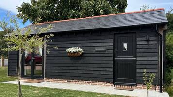 A black wooden building with a red roof, a nameplate, and a window with a curtain.