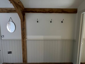 Una habitación con pared blanca de paneles, viga de techo de madera y tres ganchos en la pared.