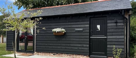 A black wooden building with a red roof, a nameplate, and a window with a curtain.