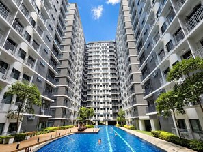 A high-rise residential building with a central swimming pool surrounded by greenery. - Stylish 1BR Near MOA • Massage Chair & Karaoke (Pasay City)