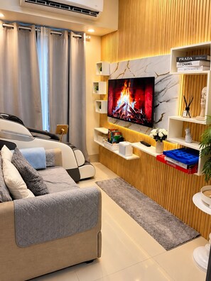 A modern living room with a sofa, TV, and wooden paneling. - Stylish 1BR Near MOA • Massage Chair & Karaoke (Pasay City)
