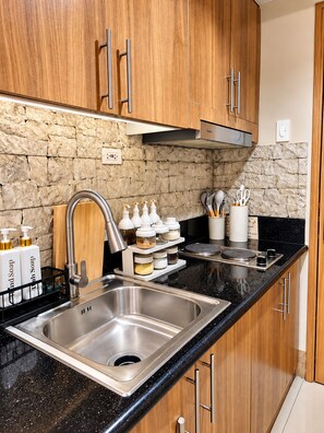 A modern kitchen with stainless steel appliances, wooden cabinets, and a stone backsplash. - Stylish 1BR Near MOA • Massage Chair & Karaoke (Pasay City)