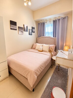 A bedroom with a bed, bedside table, lamp, and wall art. - Stylish 1BR Near MOA • Massage Chair & Karaoke (Pasay City)