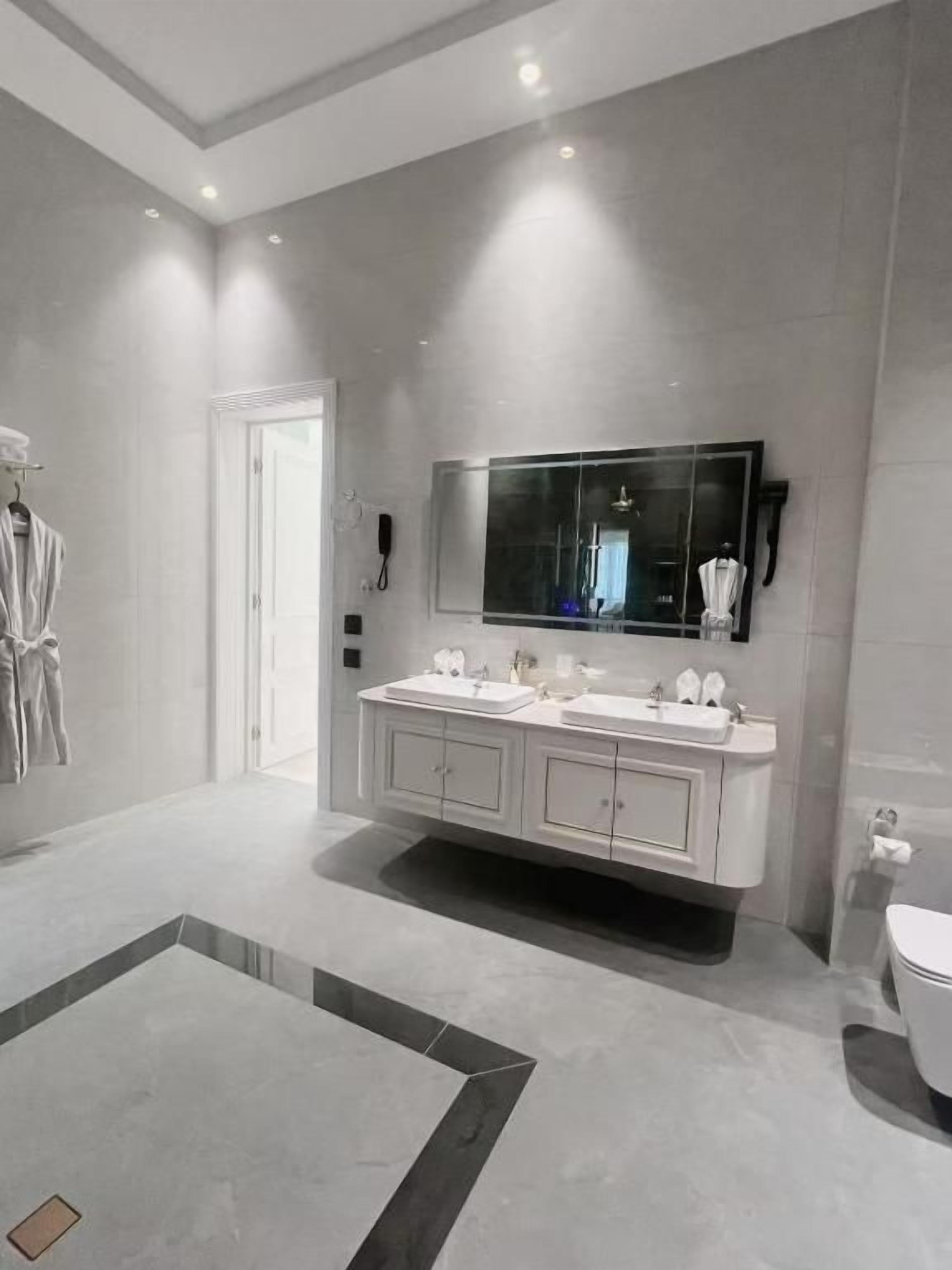 A modern bathroom with a large mirror, dual sinks, and a toilet.