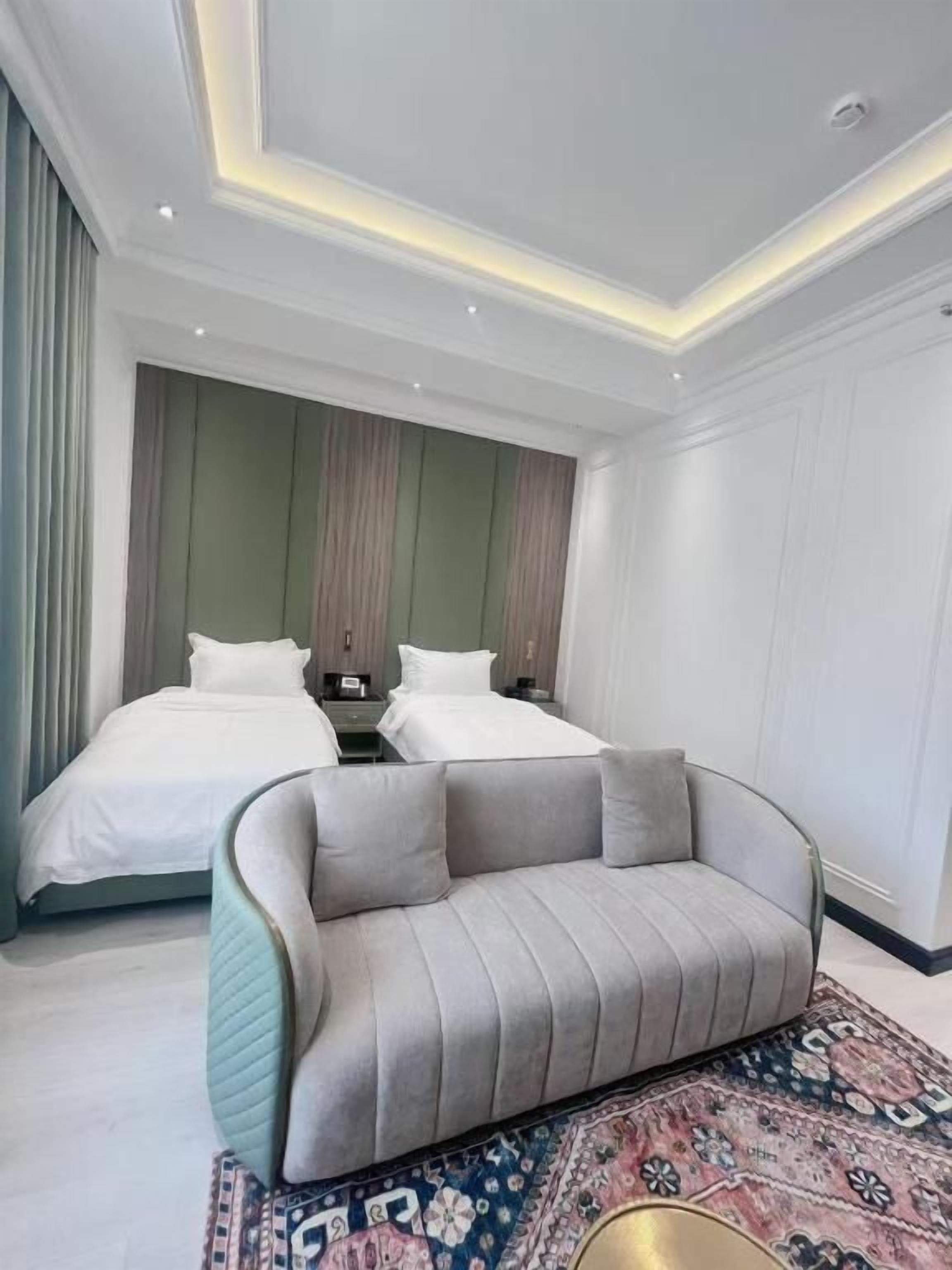 A hotel room with two beds, a sofa, a patterned rug, and a ceiling with recessed lighting.