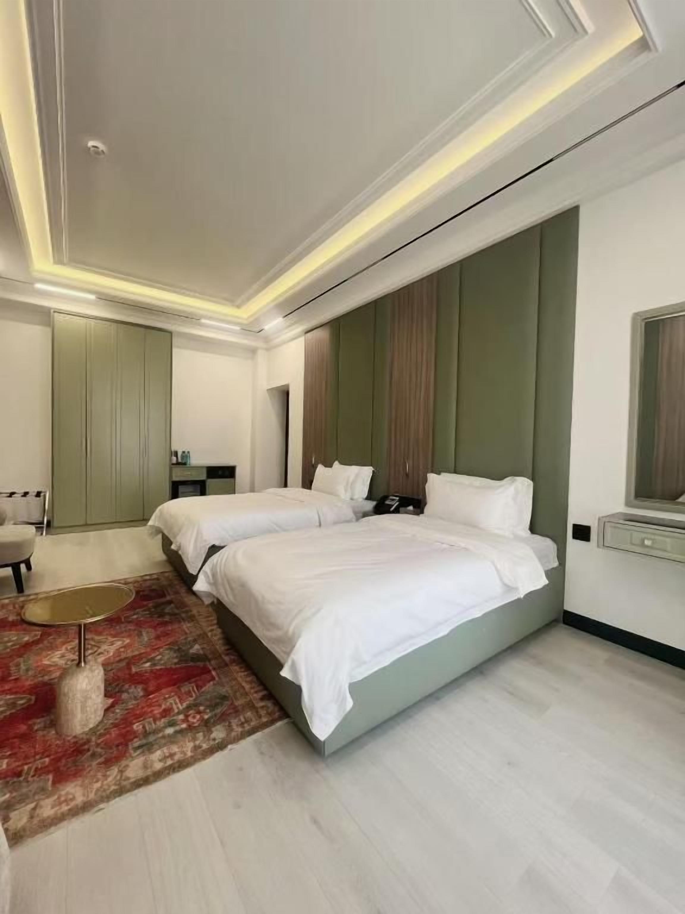 Quarto de hotel moderno com duas camas, área de estar e um espelho grande.