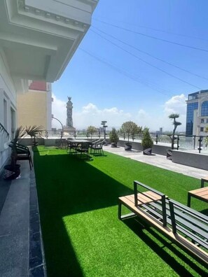 A rooftop terrace with artificial grass, outdoor furniture, and a statue in the background.