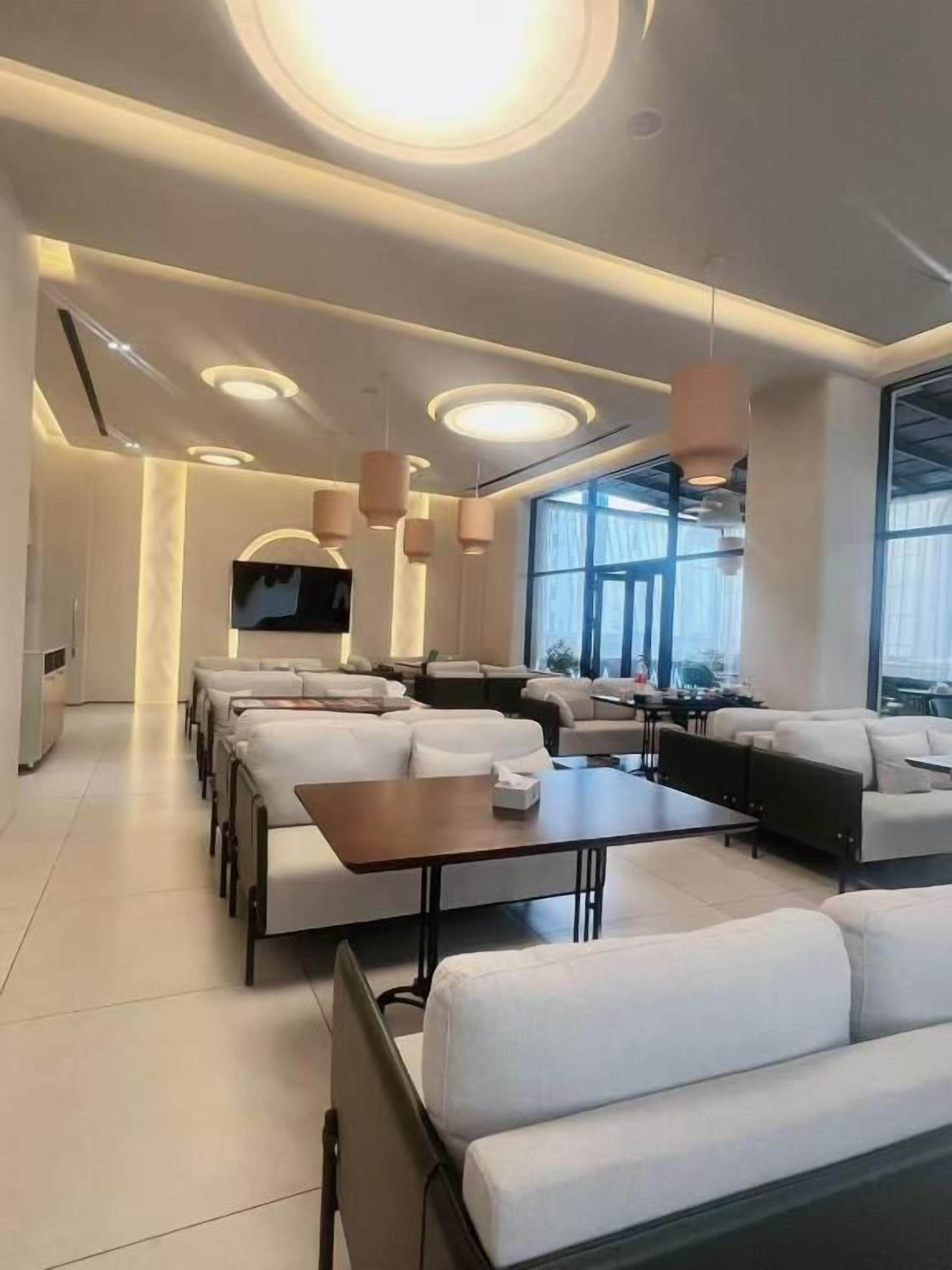 A modern lounge area with sofas and tables, large windows, and recessed ceiling lighting.
