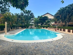A swimming pool with a stone-tiled deck, surrounded by palm trees and a building in the background. - Tremendous 3-bedroom plus one bed loft condo with AC in Las Terrenas (Las Terrenas)