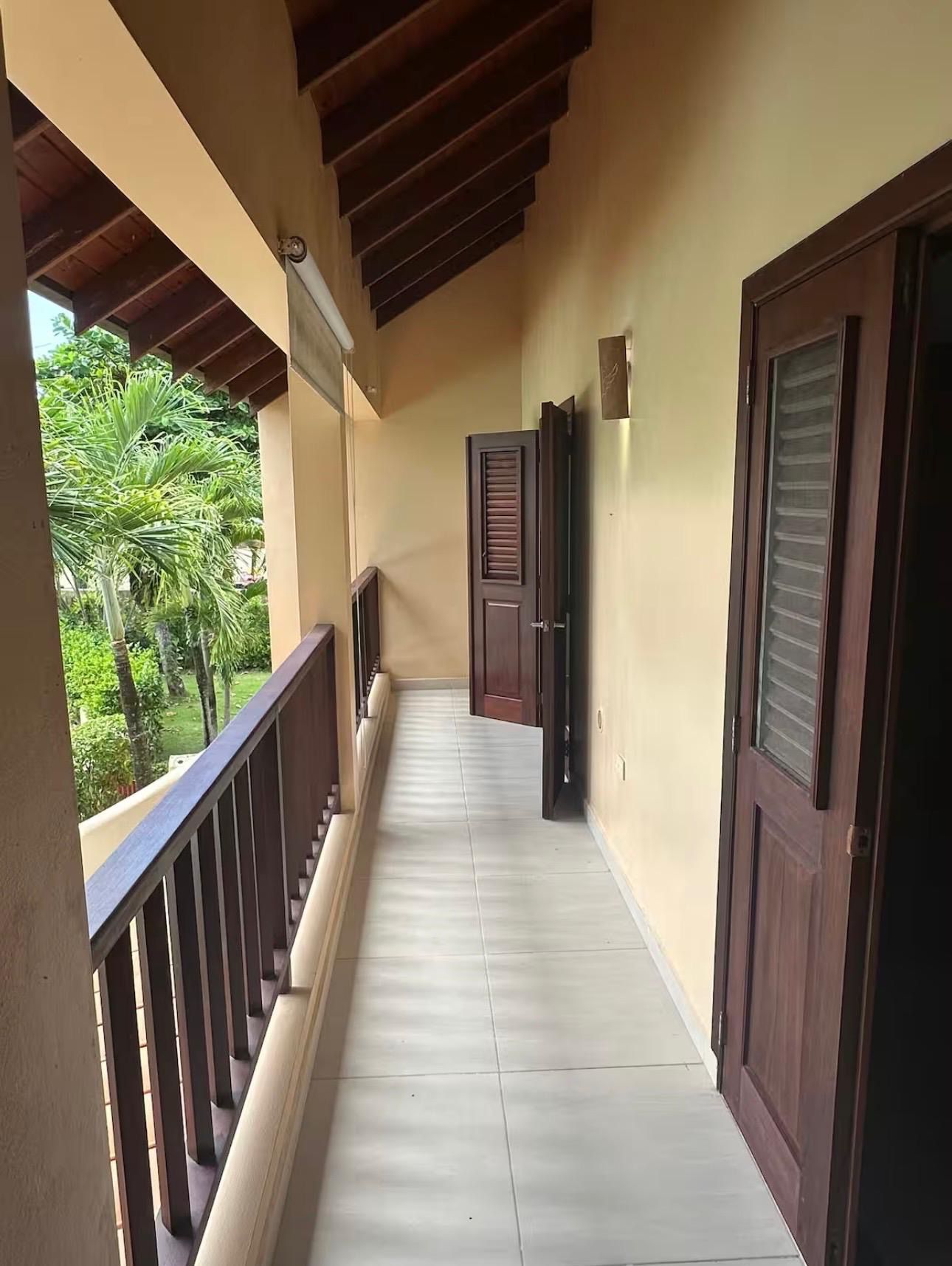 A corridor with a wooden railing, a door with a window, and a view of greenery outside.