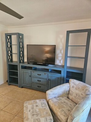 Ein Wohnzimmer mit Fernseher auf einem Holzschrank, einem gemusterten Sessel und einem Fliesenboden.