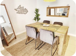 A dining area with a wooden table, four chairs, a large mirror, and a decorative wall piece. - Enjoyable 1-bedroom apartment in vibrant Bloubergstrand (Cape Town)