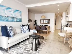 A modern living room with a sofa, coffee table, and a painting of sailboats. - Enjoyable 1-bedroom apartment in vibrant Bloubergstrand (Cape Town)