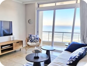 Ein modernes Wohnzimmer mit Fernseher, einem Sessel, einer Couch und Blick auf den Ozean.
