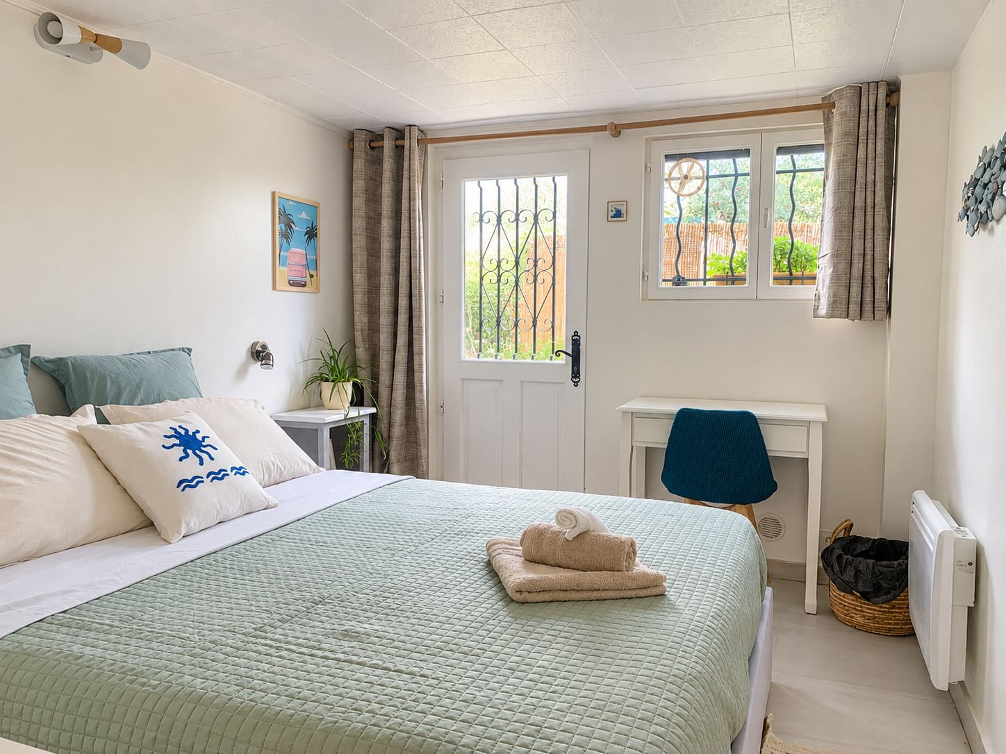 A bedroom with a bed, a desk, a chair, a radiator, and a window with curtains.