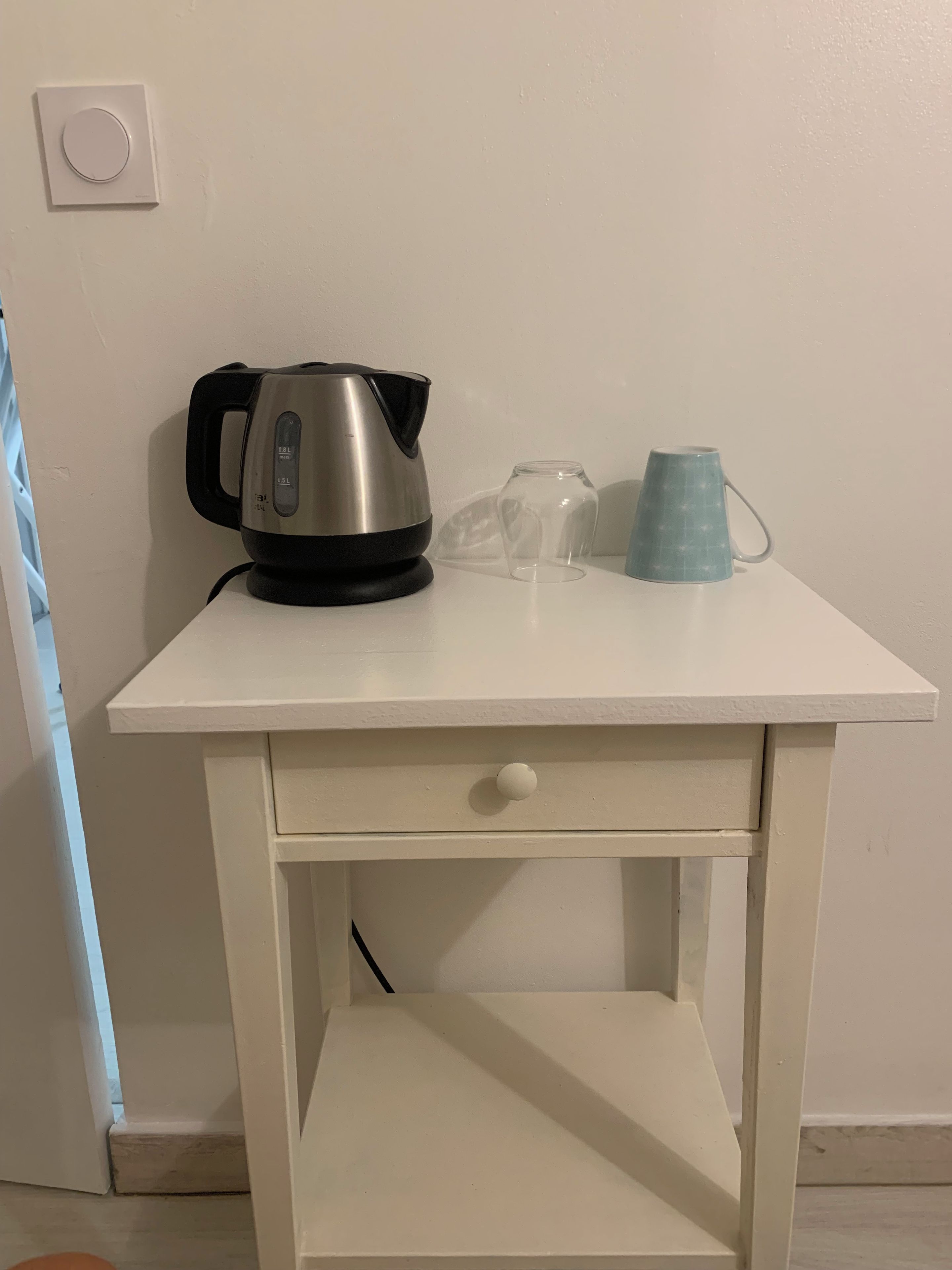 Une table blanche sur laquelle se trouvent une bouilloire, un verre et une tasse.