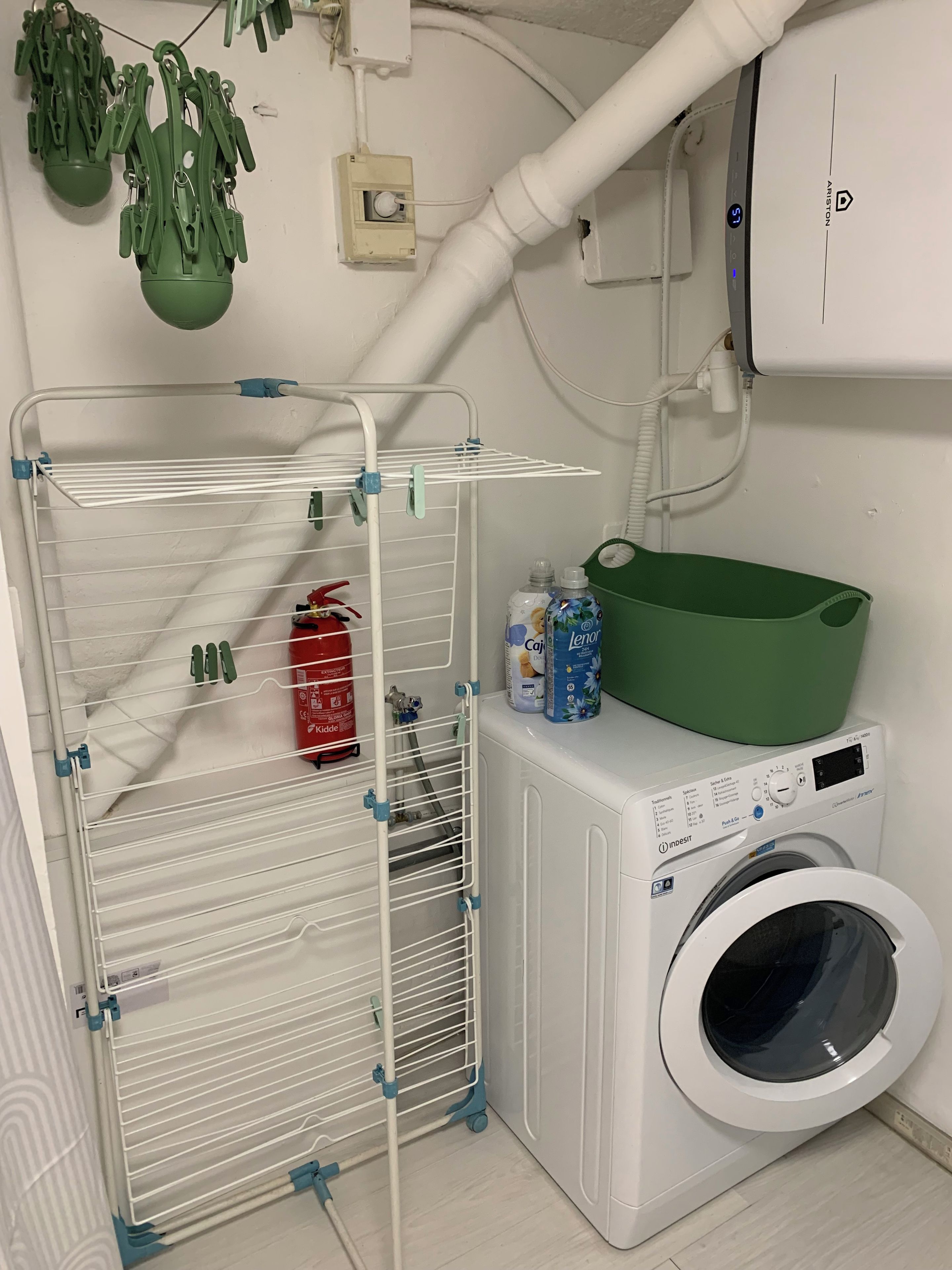 A laundry area with a white washing machine, a drying rack, and a green basket.