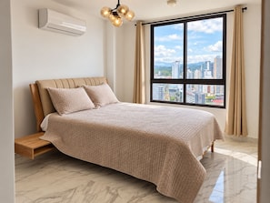 A bedroom with a bed, an air conditioning unit, a window with a city view, and a hanging light fixture. - Cozy 1-bedroom apartment in perfect Panamá with AC and gym access (Panamá)