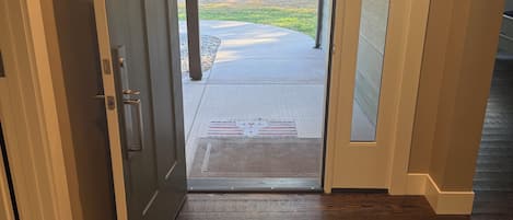 A wooden floor leading to a door with a glass panel, a welcome mat, and a view of a yard with trees and a fire pit.