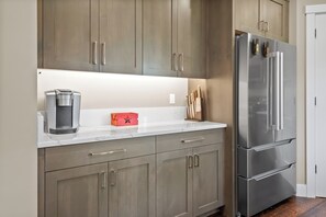 A kitchen with a stainless steel refrigerator, a coffee maker, and a red box on the counter. - Freedom House on Swan River - 3BR/2BA (Bigfork)