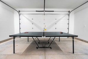 A ping pong table with a metal frame and wheels, set in a room with white walls and a concrete floor. - Freedom House on Swan River - 3BR/2BA (Bigfork)