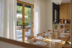 Un comedor con una mesa lista para una comida, vistas al exterior y una zona de cocina al fondo.