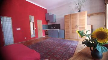 Ein Zimmer mit roter Wand, einem gemusterten Teppich, einem Bett, einem Holzschrank, einer Küchenzeile und einer Vase mit Sonnenblume.