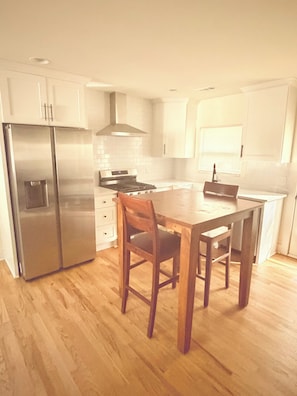 Una cocina con armarios blancos, un refrigerador de acero inoxidable, una mesa de comedor de madera y un horno empotrado.