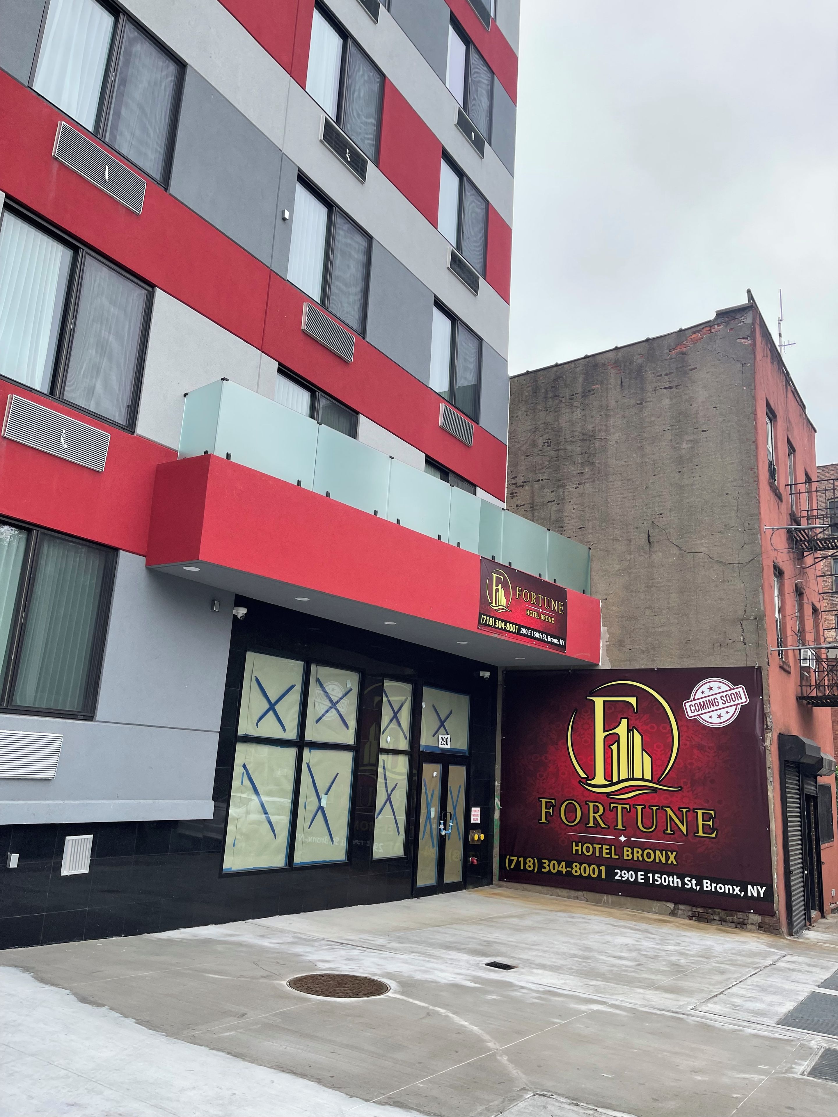 A multi-story building with a prominent 'FORTUNE HOTEL BRONX' sign, large windows with 'X' markings, and a fire sprinkler visible on the ground floor.