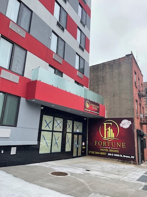 A multi-story building with a prominent 'FORTUNE HOTEL BRONX' sign, large windows with 'X' markings, and a fire sprinkler visible on the ground floor. - Fortune Hotel Bronx  (Bronx)