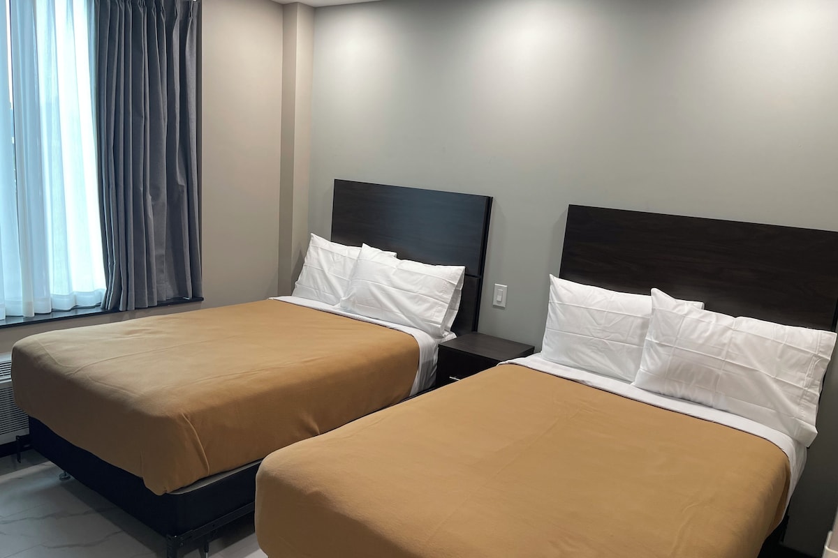 Two single beds with headboards, a window with curtains, and a light switch on the wall.