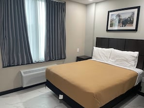A hotel room with a bed, a nightstand, a framed picture on the wall, and a window with curtains. - Fortune Hotel Bronx  (Bronx)
