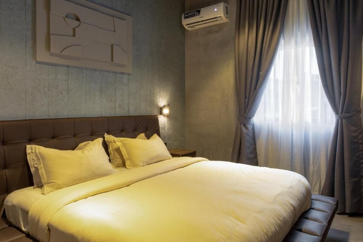 Habitación de hotel con una cama grande, cabecera, aire acondicionado instalado en la pared y una ventana con cortinas.