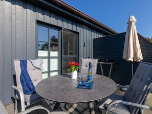 An outdoor patio with a round table, chairs, a bottle of wine, and a vase with flowers. - Holiday Apartment With 1 Bedroom (Zingst)