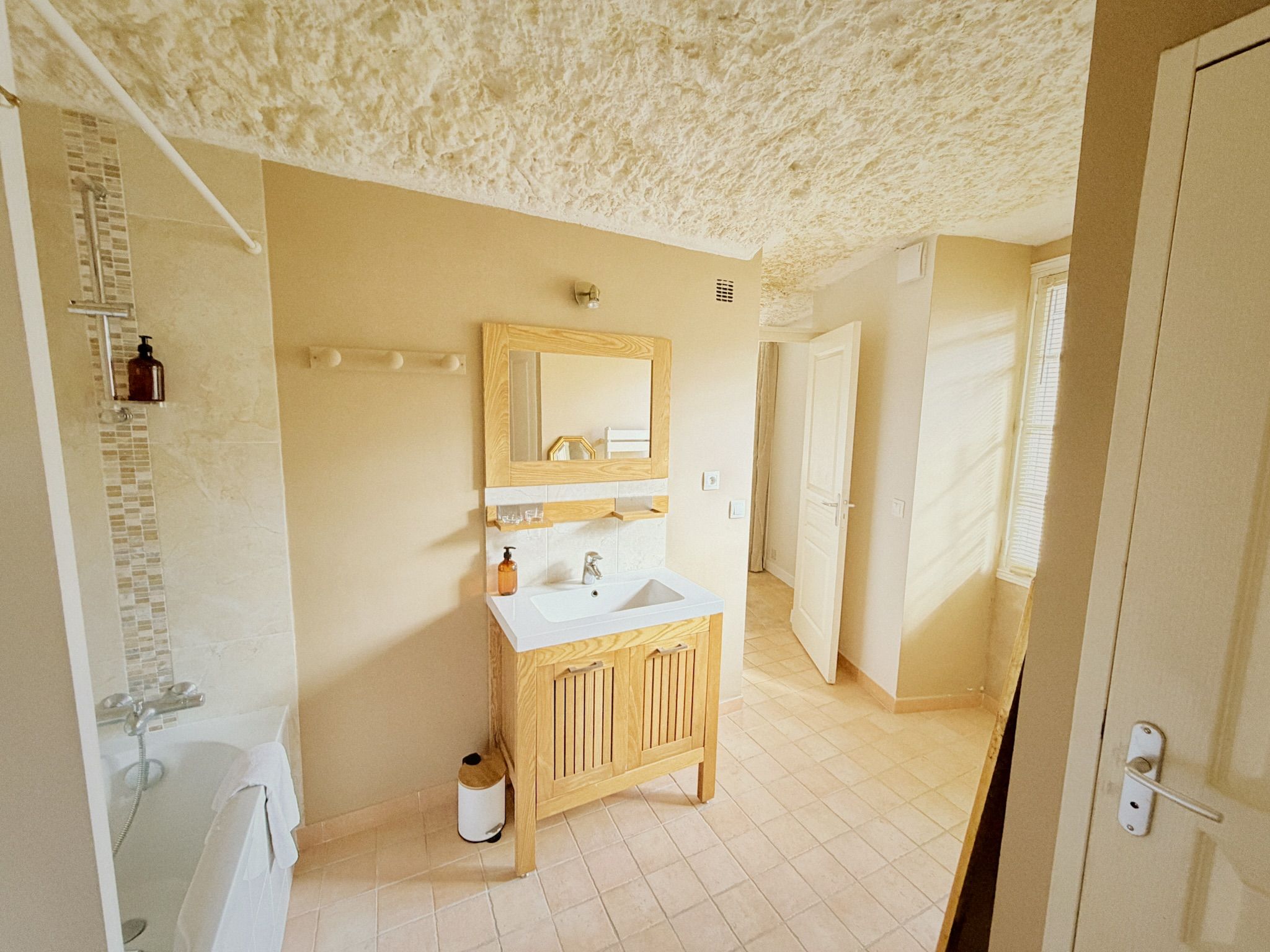 Une salle de bain avec un meuble-lavabo en bois, un miroir, un évier et un espace douche.