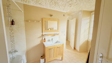 Une salle de bain avec un meuble-lavabo en bois, un miroir, un évier et un espace douche.