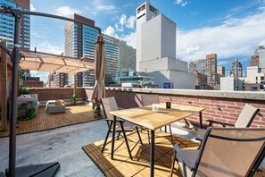 Eine Dachterrasse mit Holztisch und -stühlen, einer gepolsterten Sitzecke und Blick auf die Stadtlandschaft.