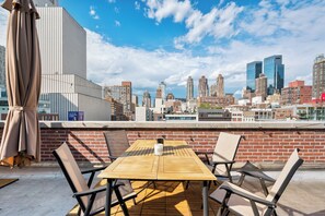 Eine Dachterrasse mit Holztisch und -stühlen, einer Ziegelwand und Blick auf den Stadtgürtel.
