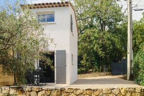 Edifici de dues plantes amb mur de pedra al fonament, un balcó amb taula i cadires, i una porta amb persianes.
