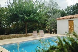 Una piscina amb dues gandules i un edifici petit amb teulada d'àmfores.